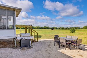 A patio with a grill, outdoor seating, and a view of a field with cows. - Fire Pit, Deck, Yard! Home Near Canadian Lakes (Mecosta)