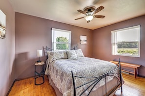 A bedroom with a bed, two windows, a ceiling fan, a bedside table, and a bench. - Fire Pit, Deck, Yard! Home Near Canadian Lakes (Mecosta)