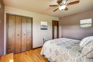 A bedroom with a wooden wardrobe, a bed with a patterned bedspread, and a ceiling fan. - Fire Pit, Beautiful Wooded View, 70 Huntable Acres (Mecosta)