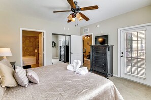 Ein Schlafzimmer mit einem Bett, einem Deckenventilator, einem Schminktisch, einem Fernseher und einem durchgegangenen Tür sichtbaren Badezimmer.