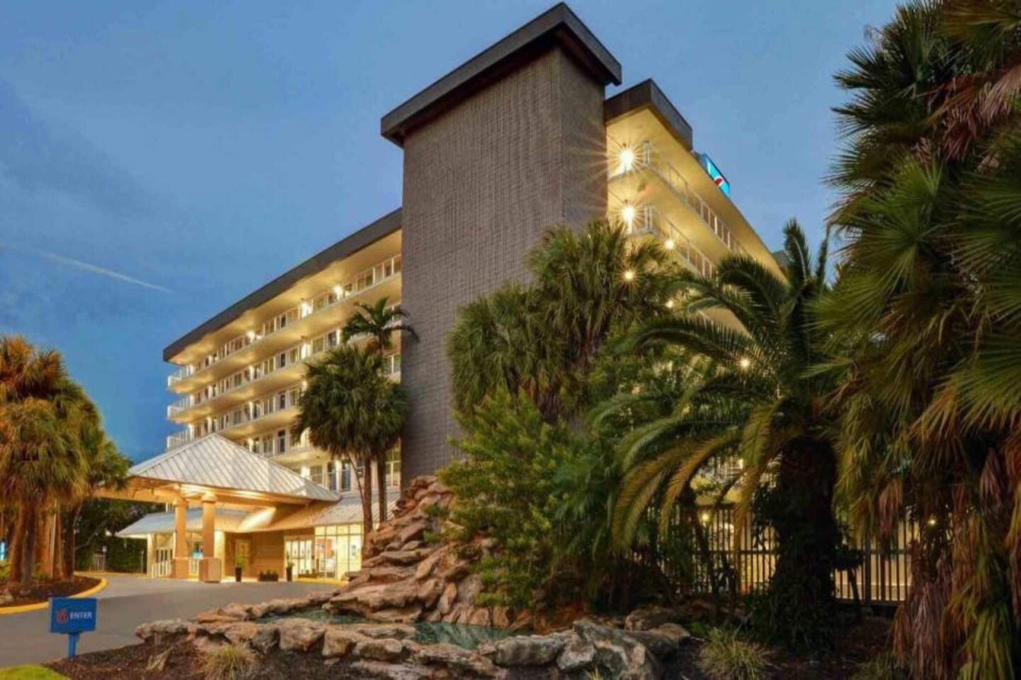 A multi-story hotel with a prominent entrance, palm trees, and a rocky landscape.
