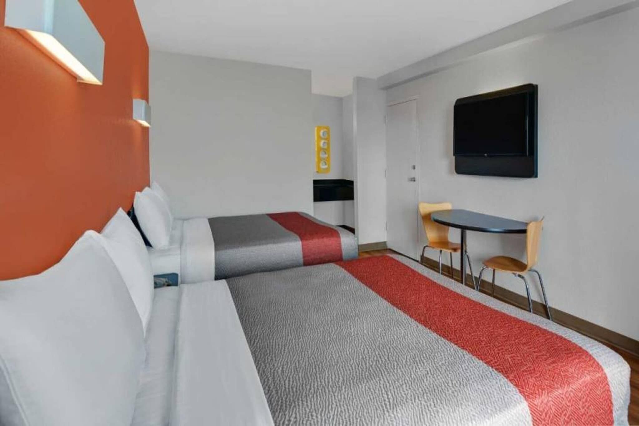 A hotel room with two beds, a desk, a chair, a television, and a wall-mounted control panel.