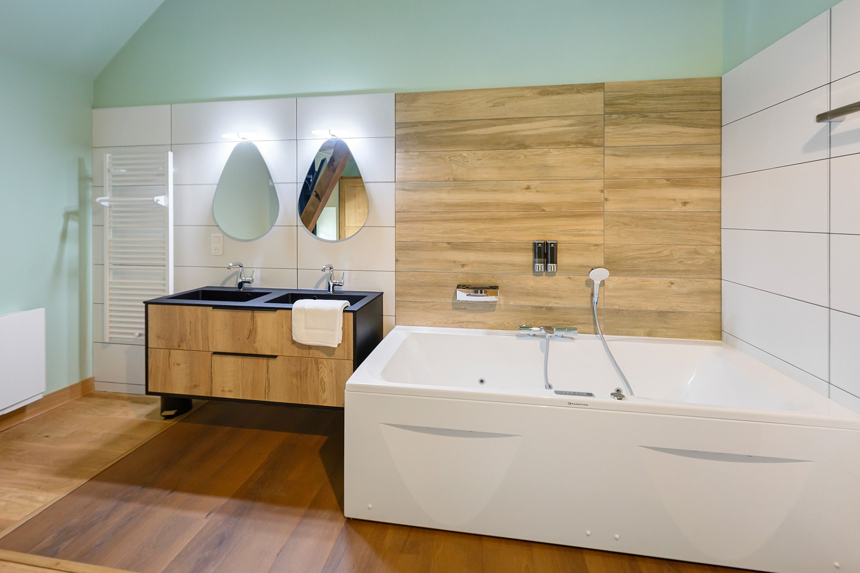 Un baño moderno con tocador de madera, un espejo grande, una bañera y un perchero para toallas.