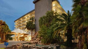 Un hotel de varios pisos con una entrada destacada, palmeras y un paisaje rocoso.