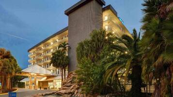 Ein mehrstöckiges Hotel mit einer markanten Eingangspartie, Palmen und einer felsigen Landschaft.