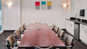 Un salón de conferencias con una larga mesa, sillas y una kitchenette.