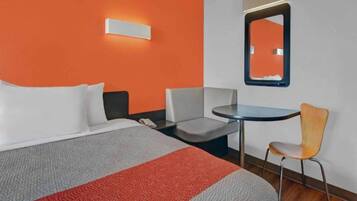 A hotel room with a bed, a desk, a chair, and a mirror.