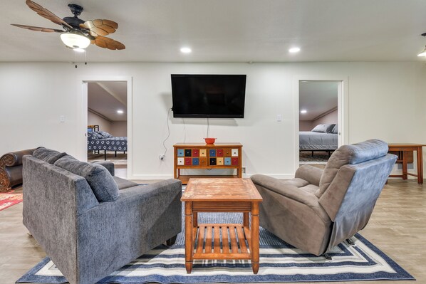 A living room with a flat-screen TV mounted on the wall, a ceiling fan, and a wooden coffee table.