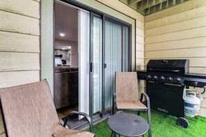 A patio area with a grill, two chairs, and a sliding glass door leading to a kitchen. - Walkable Condo Near Ski Shuttle & Mammoth Creek! (Mammoth Lakes)