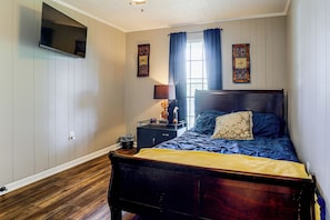 A bedroom with a wooden bed, a nightstand, a lamp, and a wall-mounted TV.
