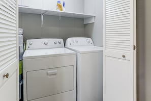 A laundry room with two stacked washers and dryers, a shelf above with cleaning supplies, and a door with a brass handle.