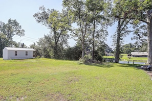 A grassy area with a small white building, trees, and a distant house.