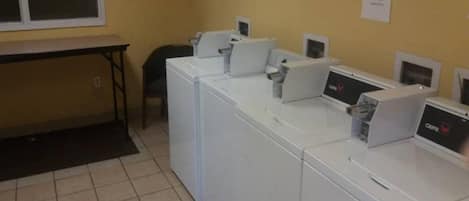 Un cuarto de lavandería con varias lavadoras y secadoras, una mesa y sillas.