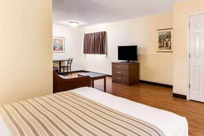Quarto de hotel com cama, escrivaninha, cadeira, televisão e guarda-roupa.