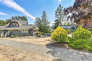 A two-story building with a sloped roof, a front porch, and a driveway leading to a parking area.