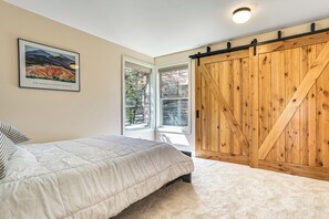 A bedroom with a large bed, a wooden wardrobe, a window with a view of trees, and a framed picture on the wall.