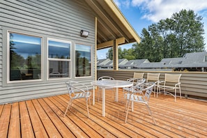 A wooden deck with a table and chairs, large windows, and a covered area with a view of trees.