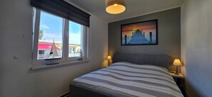A hotel room with a bed, a window with a view, a painting on the wall, and a lamp on the nightstand. - KWU 10 OG Vacation Rental - "Coastal Oasis" - The Ultimate Vacation: Your Modern 4-Star (Gelbensande)