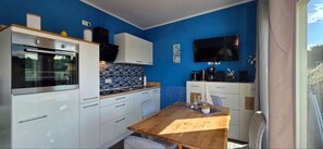 A compact kitchen with white cabinets, a built-in oven, a tiled backsplash, and a wooden dining table. - KWU 10 OG Vacation Rental - "Coastal Oasis" - The Ultimate Vacation: Your Modern 4-Star (Gelbensande)