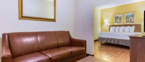 Una habitación de hotel con un sofá de cuero marrón, una mesa de centro de madera, una cama con ropa de cama blanca y una mesita de noche.