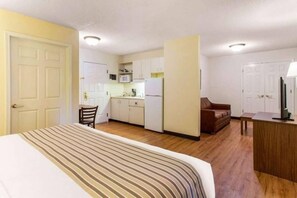 Une chambre d’hôtel de taille réduite comprenant un lit, une kitchenette, un coin salon et un téléviseur.
