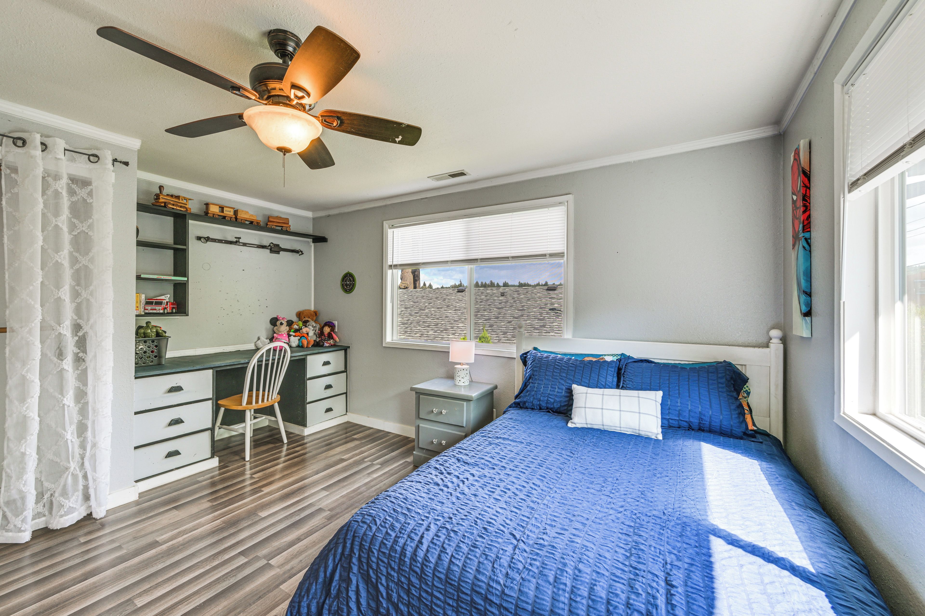 Un dormitorio con cama, escritorio, silla, ventana y ventilador de techo.