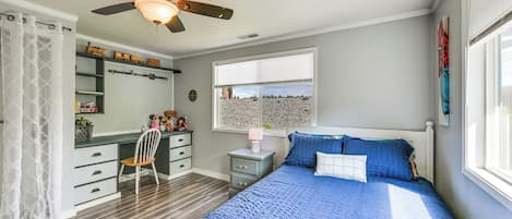 Une chambre à coucher comprenant un lit, un bureau, une chaise, une fenêtre et un ventilateur de plafond.
