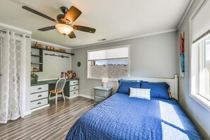 Quarto com cama, escrivaninha, cadeira, janela e ventilador de teto.
