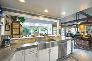 A spacious kitchen with a large island, modern appliances, and a view of a lakeside patio. - Waterfront Living on Lake St Clair with Sauna (Olympia)