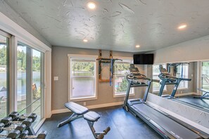 Une salle de sport équipée de matériel d’exercice, dotée de grandes fenêtres et offrant une vue sur un lac.