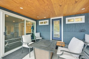 A covered patio area with a table and chairs, a sliding glass door, and a blue wall with windows. - Waterfront Living on Lake St Clair with Sauna (Olympia)