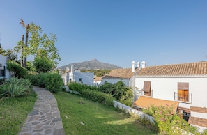 A pathway leading to a white building with a tiled roof, surrounded by greenery and a mountain in the background. - Marbella gateway - 2BR House /w AC, Patio and Pool Surrounded by Golf Courses (Marbella)