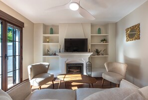 A living room with a fireplace, two armchairs, a coffee table, and a television. - Marbella gateway - 2BR House /w AC, Patio and Pool Surrounded by Golf Courses (Marbella)