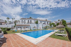 A pool area with a clear blue pool, white buildings, and palm trees. - Marbella gateway - 2BR House /w AC, Patio and Pool Surrounded by Golf Courses (Marbella)