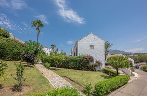 A white building with a stone pathway leading to it, surrounded by greenery and palm trees. - Marbella gateway - 2BR House /w AC, Patio and Pool Surrounded by Golf Courses (Marbella)