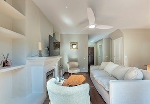 A living room with a fireplace, a ceiling fan, a sofa, and a coffee table. - Marbella gateway - 2BR House /w AC, Patio and Pool Surrounded by Golf Courses (Marbella)