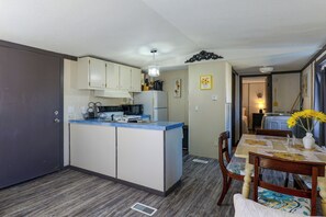 A compact kitchen with a microwave, toaster, and a sink. There is a dining area with a table and chairs, and a vase with flowers on the table. - Fort Stockton Home, Your Big Bend Basecamp (Fort Stockton)