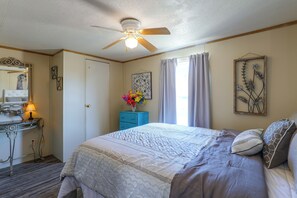 A bedroom with a bed, a dresser, a vanity, and a ceiling fan.