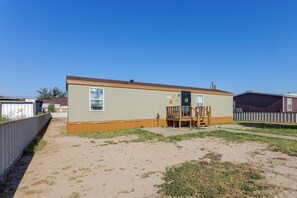 A single-story mobile home with a fenced yard, a small deck, and a window. - Fort Stockton Home, Your Big Bend Basecamp (Fort Stockton)