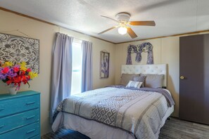 A bedroom with a bed, a ceiling fan, a window with curtains, a dresser, and a vase of flowers. - Fort Stockton Home, Your Big Bend Basecamp (Fort Stockton)