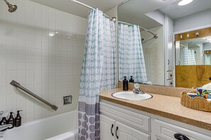 Un baño con bañera, lavamanos con artículos de aseo, espejo y cortina de ducha.