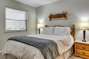 Un dormitorio con cama, mesitas de noche, una ventana con persianas y un estante en la pared.