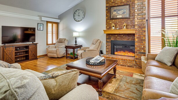 A living room with a fireplace, leather sofas, a television, and a clock on the wall. - Patio & Courtyard! Elk City Townhome (Elk City)