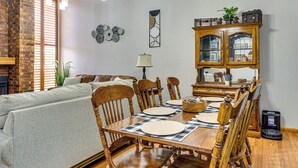 A dining area with a wooden table set for four, flanked by chairs, a chandelier, and a cabinet with glass doors. - Patio & Courtyard! Elk City Townhome (Elk City)