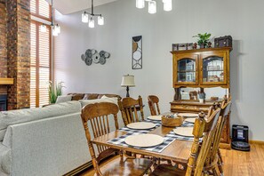 Un comedor con una mesa de madera dispuesta para cuatro personas, flanqueada por sillas, una lámpara de araña y un aparador con puertas de cristal.