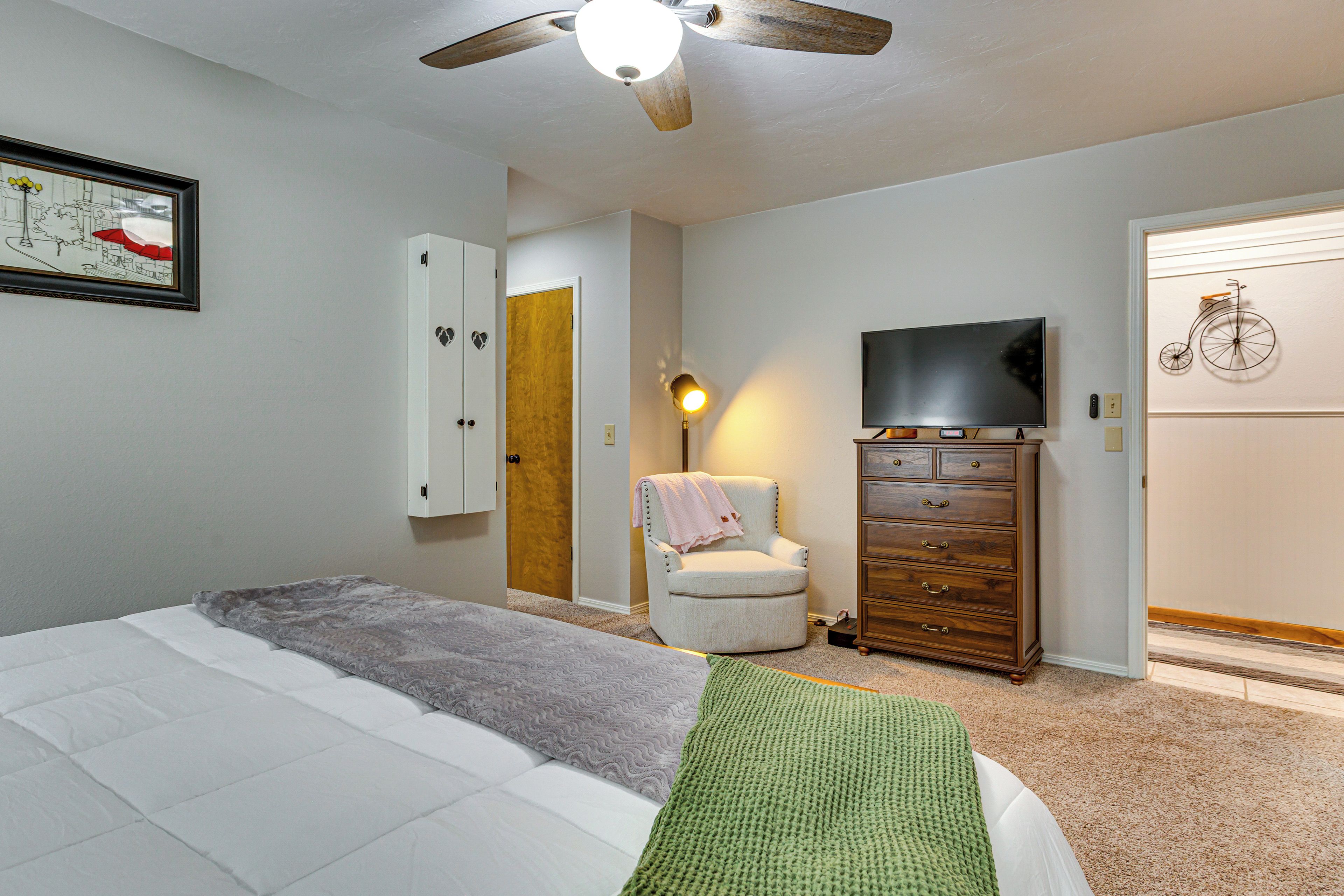 Une chambre à coucher comprenant un lit, une chaise, une commode, un téléviseur et un ventilateur de plafond.