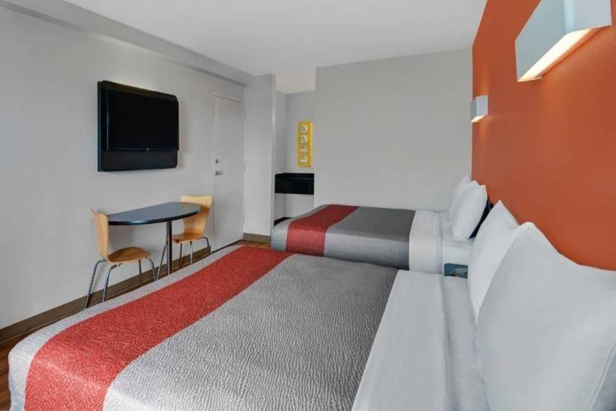 A hotel room with two beds, a desk, a chair, a television, and a wall-mounted control panel.