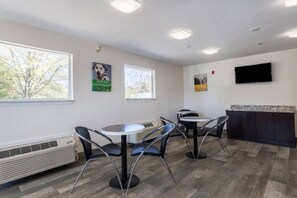 Una habitación con una mesa redonda, sillas, un televisor de pantalla plana en la pared y una ventana con vistas a árboles.