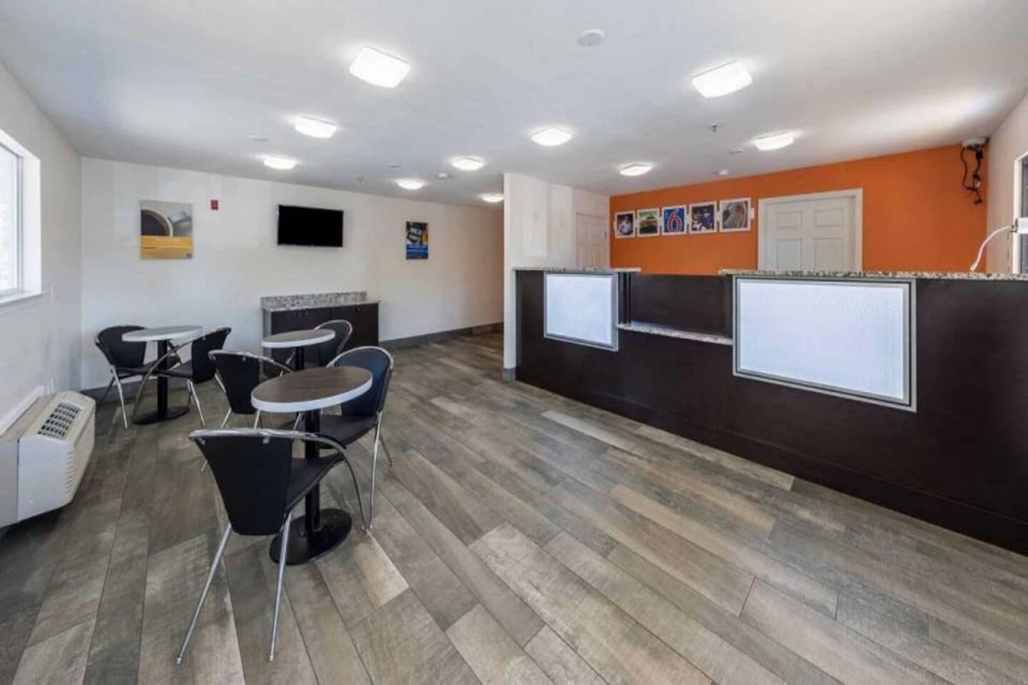 A modern office space with a reception area, several tables and chairs, and a flat-screen TV mounted on the wall.