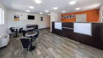 A modern office space with a reception area, several tables and chairs, and a flat-screen TV mounted on the wall.
